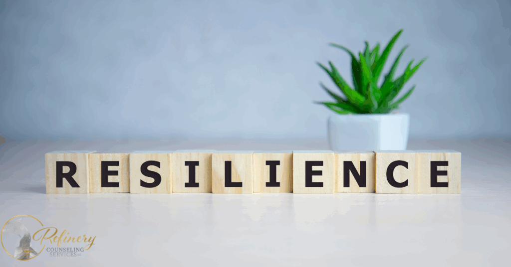 Wooden blocks spelling “resilience” on a table with a small potted plant in the background, symbolizing emotional strength and personal growth.