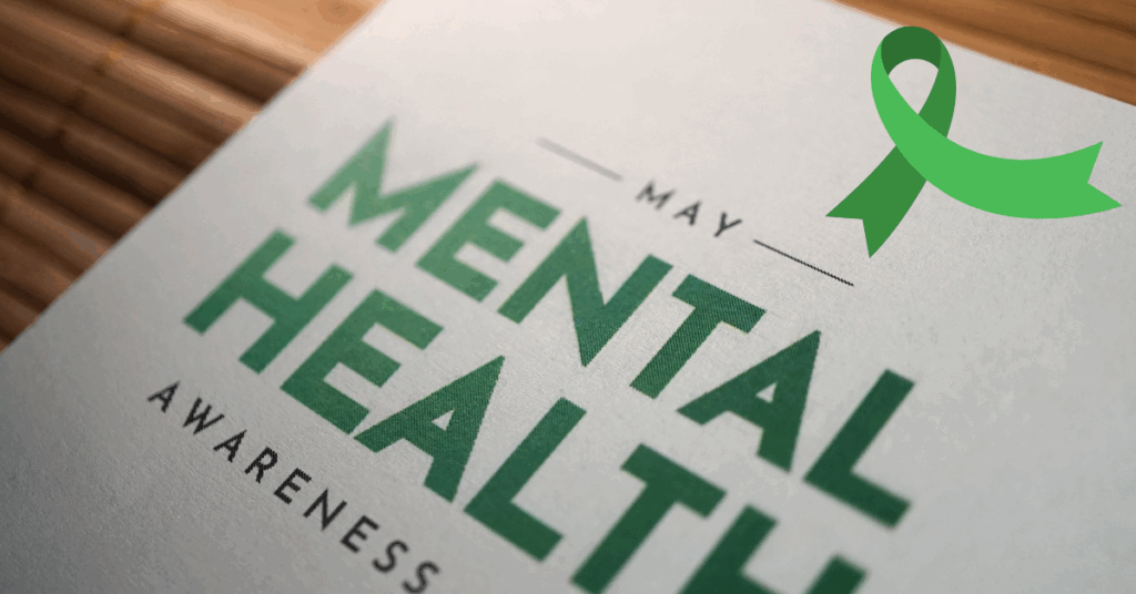 Close-up of a sign that reads 'May Mental Health Awareness' with a green awareness ribbon, symbolizing Mental Health Awareness Month