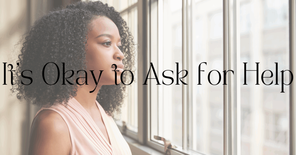 A woman gazing out of a window with soft light streaming in, overlaid with the words “It’s okay to ask for help”—conveying reflection, vulnerability, and encouragement to seek mental health support.
