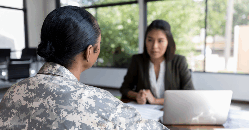 A professional woman sitting across from a military service member and a laptop on the desk signifying veterans returning to work