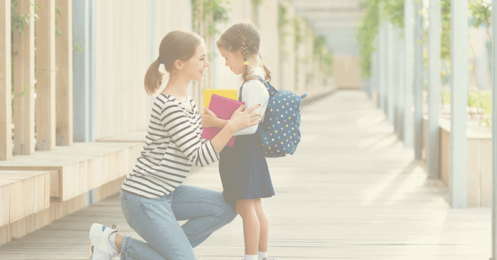 Mother kneeling with child carrying school books representing first day of school anxiety.