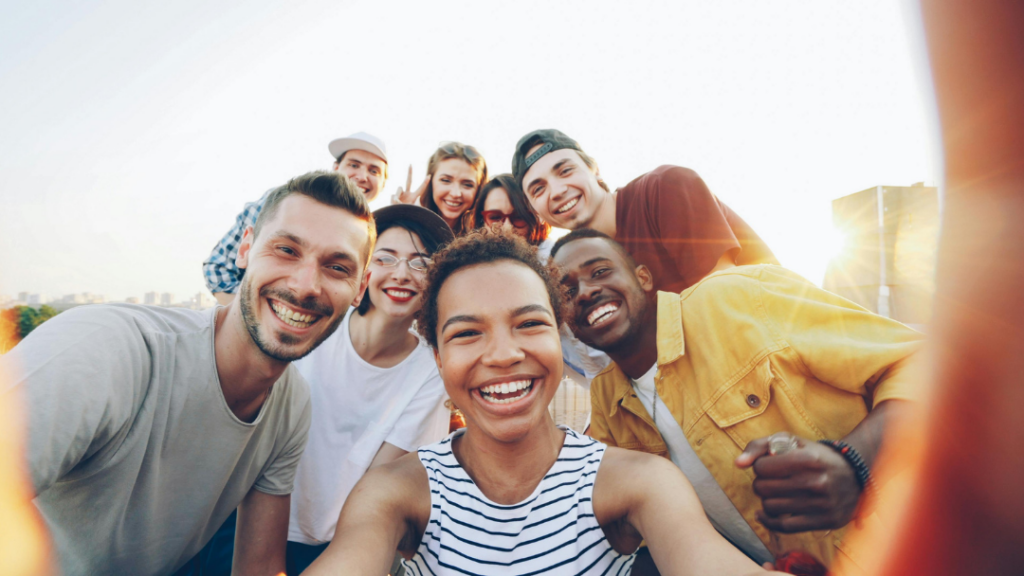 What It Means to Truly Support Mental Health — For Yourself and Others - Group of smiling friends posing for a selfie outdoors, sunlight behind them, diverse group sharing a fun moment.
