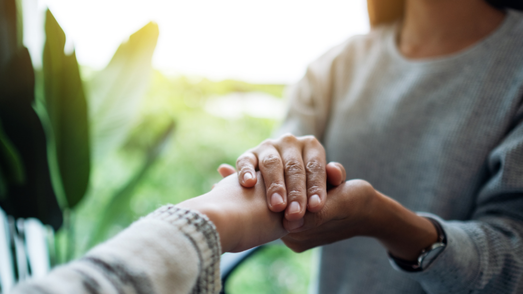 How Trauma Can Change the Way People Give and Receive Love - Two people hold hands in a supportive gesture outdoors, conveying care and connection