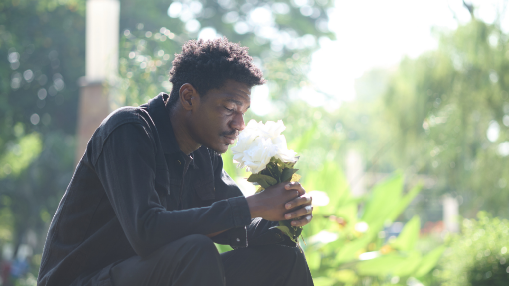 Man sitting in a sunny garden, smelling a bouquet of white roses in his hands.