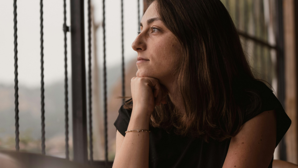 Woman with brown hair rests her chin on her hand gazing thoughtfully through a railing outdoors