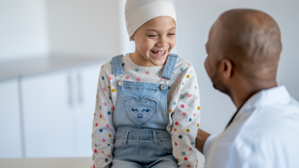 Young girl in a head wrap and polka dot sweater laughs with a male doctor in a clinic