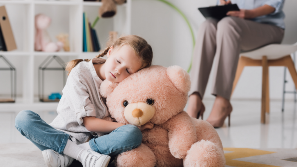 Helping Children Cope With a Loved Ones Serious Illness Young girl sleeping while hugging a large pink teddy bear in a bright room
