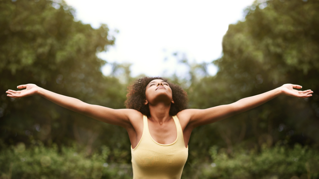 Small Signs of Emotional Growth You May Be Overlooking Woman standing outdoors with arms outstretched face tilted upward sunlight on her shoulders