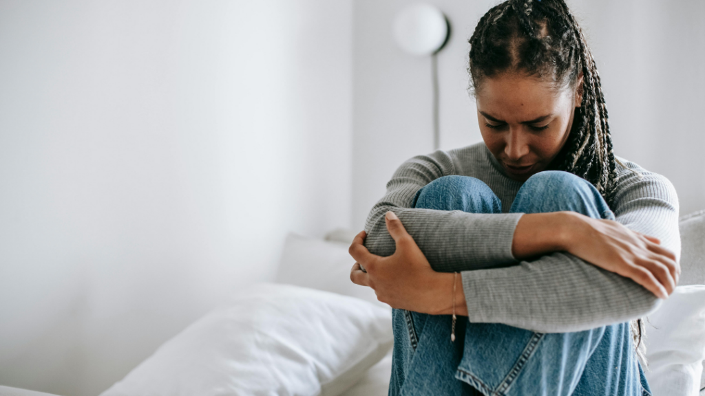 After the Relationship Ends Understanding the Psychological Aftermath of Domestic Violence Woman sitting on a bed knees drawn up to her chest arms wrapped around them head bowed in thought or sadness