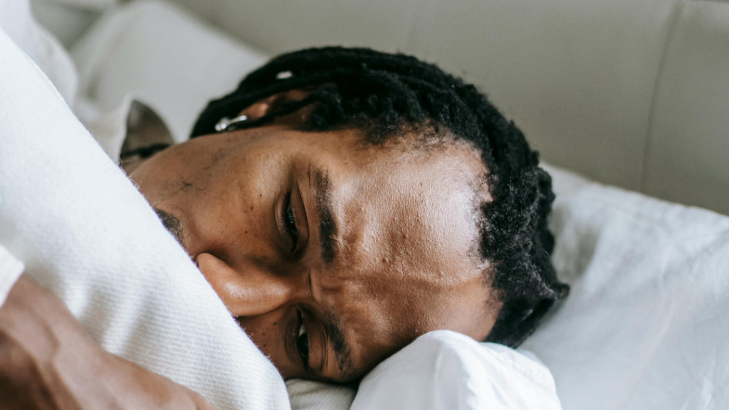 Why Your Body May Still React Like Youre in Danger After Trauma Man resting in bed with a white blanket looking tired and unwell close up of his face