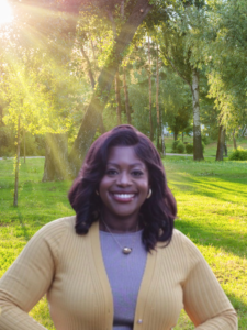 Smiling woman wearing a beige cardigan in a sunlit park with trees nearbysunlight filters through the foliage